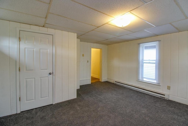 unfurnished bedroom featuring a paneled ceiling, dark carpet, and a baseboard heating unit