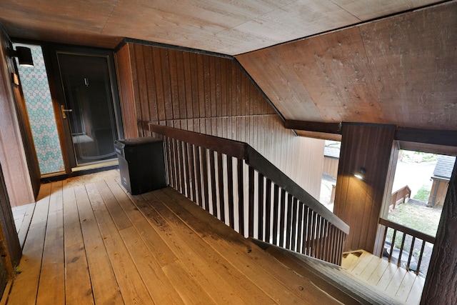 hall with wood walls, hardwood / wood-style floors, wooden ceiling, and lofted ceiling