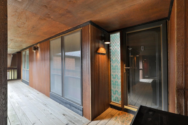 hallway featuring light wood-type flooring, wood walls, and wood ceiling