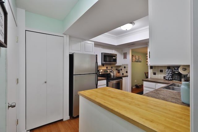 kitchen with white cabinetry, wood counters, light hardwood / wood-style flooring, backsplash, and appliances with stainless steel finishes