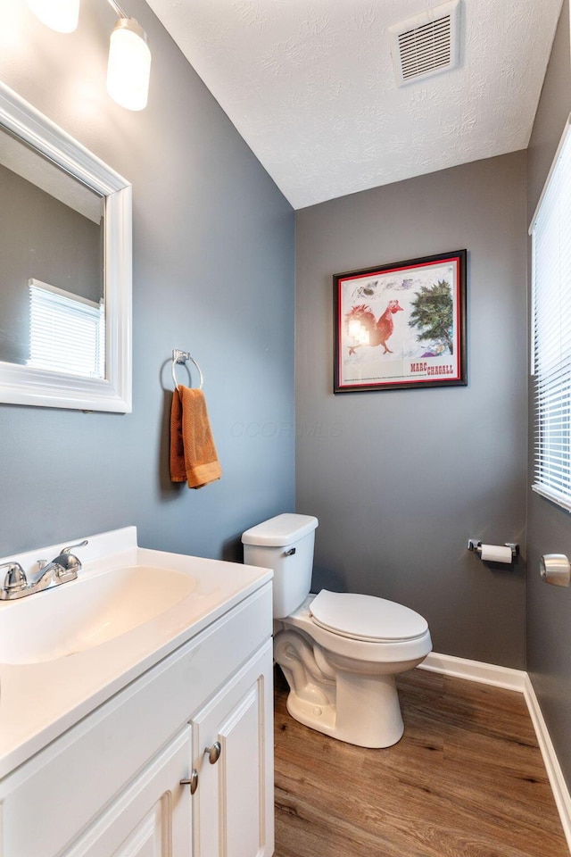 bathroom with wood-type flooring, toilet, vanity, and a textured ceiling