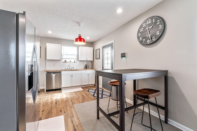 kitchen featuring appliances with stainless steel finishes, white cabinetry, sink, decorative backsplash, and hanging light fixtures