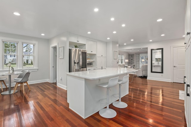 kitchen featuring stainless steel refrigerator with ice dispenser, a breakfast bar, white cabinetry, light stone counters, and a kitchen island