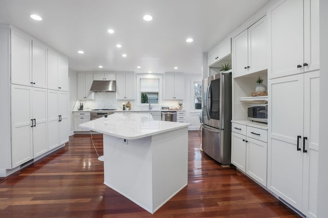 kitchen featuring appliances with stainless steel finishes, white cabinetry, a center island, tasteful backsplash, and dark hardwood / wood-style flooring