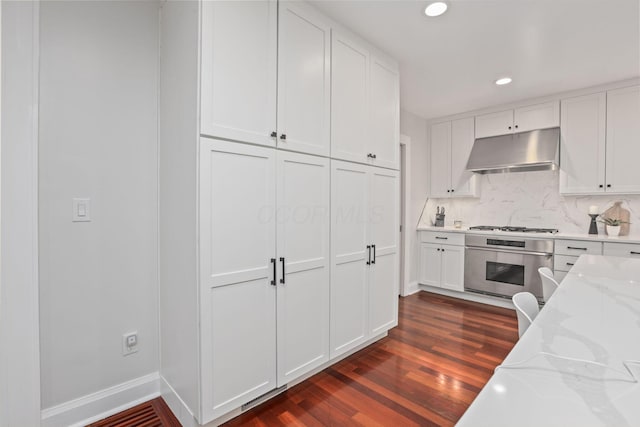 kitchen featuring white cabinetry, oven, backsplash, light stone countertops, and dark wood-type flooring