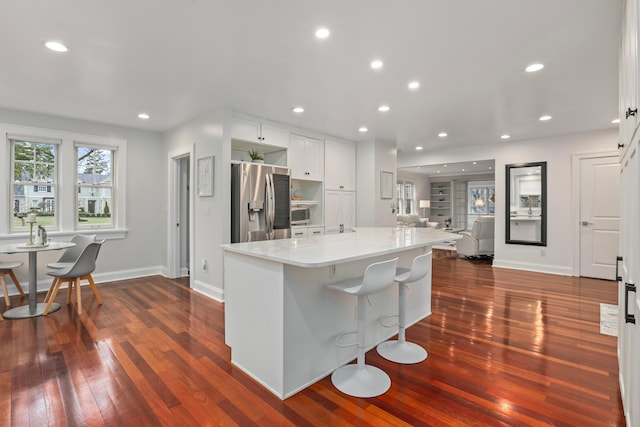 kitchen featuring white cabinetry, a kitchen breakfast bar, light stone countertops, a kitchen island, and stainless steel fridge with ice dispenser