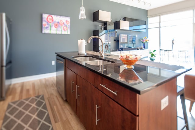 kitchen featuring appliances with stainless steel finishes, decorative light fixtures, sink, a center island with sink, and light wood-type flooring