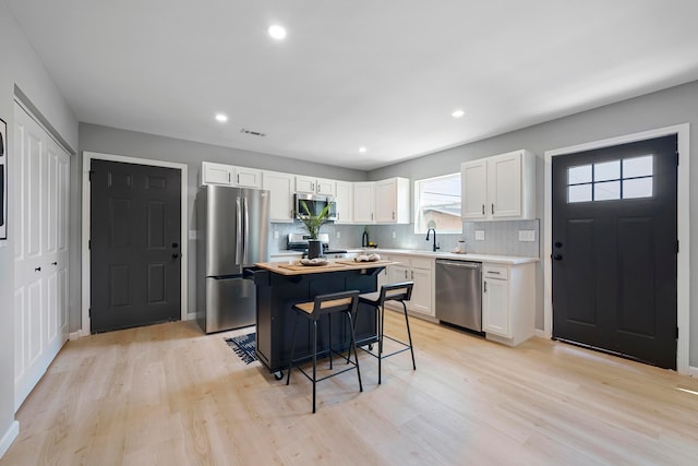 kitchen featuring white cabinets, a kitchen breakfast bar, stainless steel appliances, and light hardwood / wood-style flooring