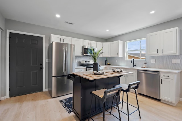 kitchen with a kitchen breakfast bar, stainless steel appliances, light hardwood / wood-style flooring, white cabinets, and a center island