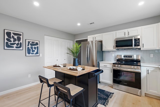 kitchen with backsplash, light wood-type flooring, white cabinetry, and stainless steel appliances