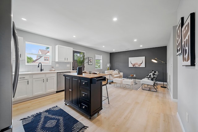 kitchen featuring stainless steel appliances, a kitchen island, a breakfast bar, white cabinets, and light wood-type flooring