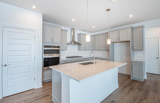 kitchen featuring wall chimney range hood, a sink, appliances with stainless steel finishes, and gray cabinetry