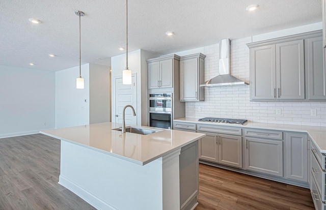 kitchen featuring dark wood-style flooring, a sink, gray cabinetry, and wall chimney exhaust hood