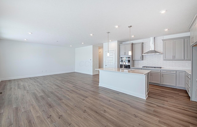 kitchen featuring decorative backsplash, wall chimney exhaust hood, gray cabinets, and light wood finished floors