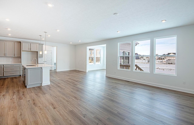 kitchen featuring light countertops, wood finished floors, a sink, open floor plan, and backsplash