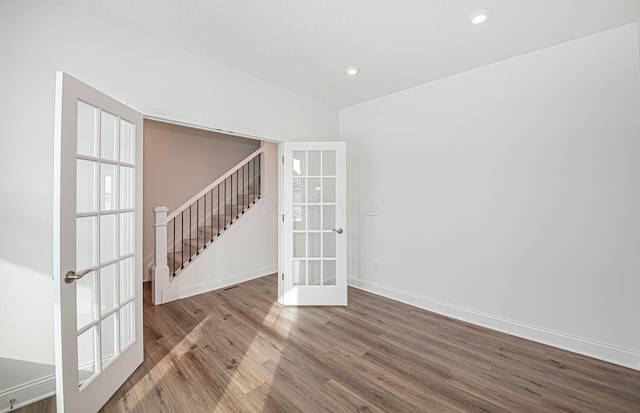 unfurnished room with baseboards, wood finished floors, french doors, and stairway
