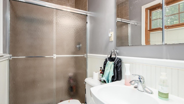 bathroom featuring toilet, a shower with door, and sink