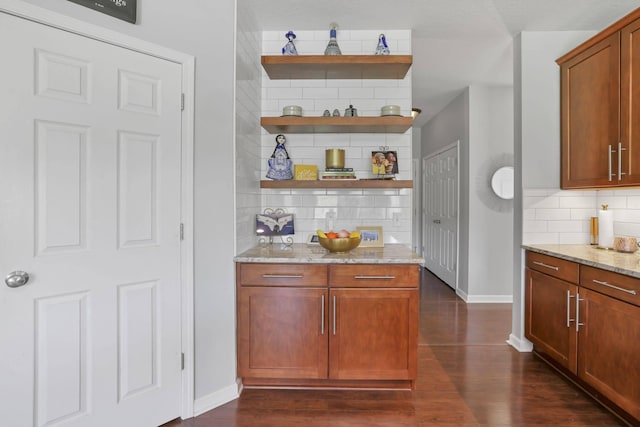 bar featuring light stone countertops, tasteful backsplash, and dark wood-type flooring