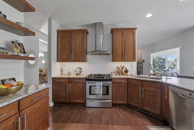 kitchen featuring light stone counters, wall chimney exhaust hood, stainless steel appliances, dark wood-type flooring, and sink