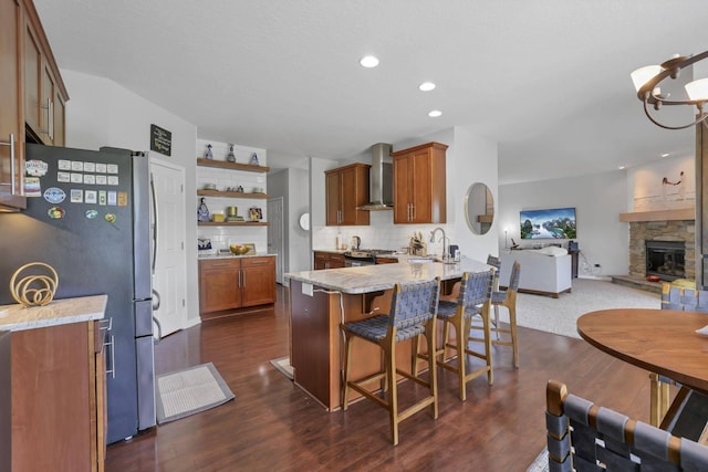 kitchen featuring kitchen peninsula, stainless steel fridge, dark hardwood / wood-style flooring, and wall chimney exhaust hood