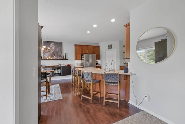 kitchen featuring sink, stainless steel refrigerator with ice dispenser, dark hardwood / wood-style floors, a kitchen bar, and kitchen peninsula