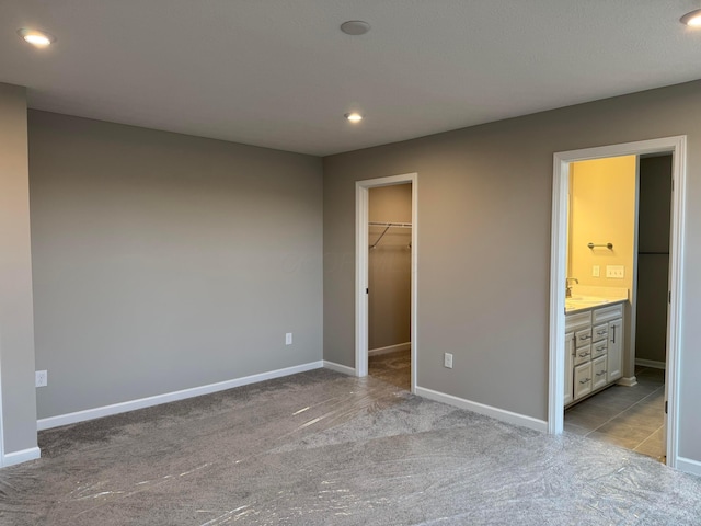 unfurnished bedroom with ensuite bath, light colored carpet, sink, a spacious closet, and a closet