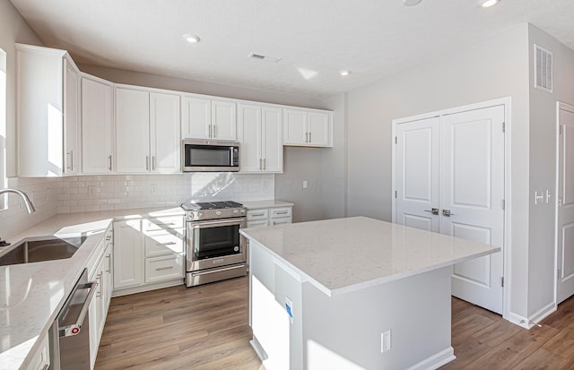 kitchen featuring white cabinetry, stainless steel appliances, a center island, light stone countertops, and sink