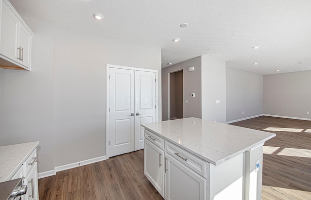 kitchen featuring hardwood / wood-style floors, white cabinetry, a kitchen island, a textured ceiling, and light stone countertops