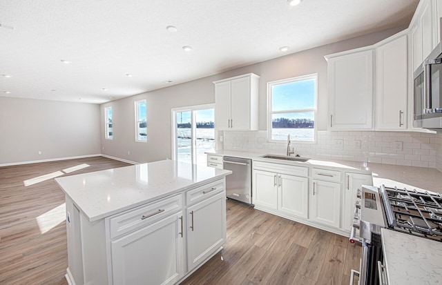 kitchen featuring appliances with stainless steel finishes, light wood-type flooring, light stone countertops, white cabinets, and sink