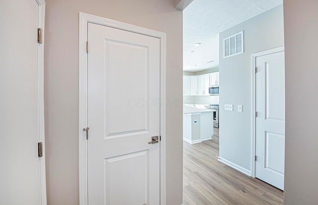 hall featuring light wood-type flooring and a textured ceiling