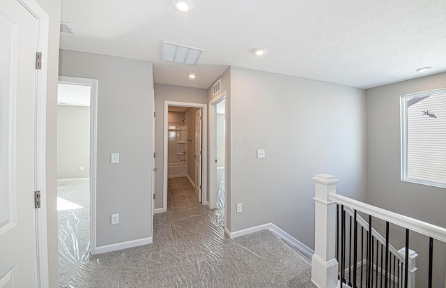 corridor featuring a textured ceiling and light colored carpet