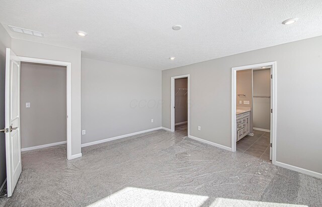 unfurnished bedroom with a textured ceiling, light carpet, connected bathroom, and a walk in closet