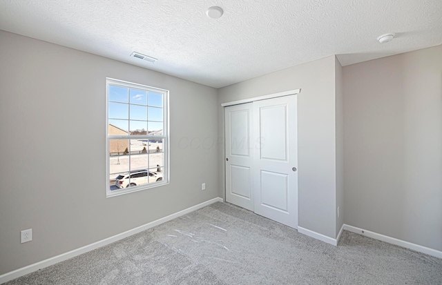 unfurnished bedroom featuring a closet, a textured ceiling, and light colored carpet