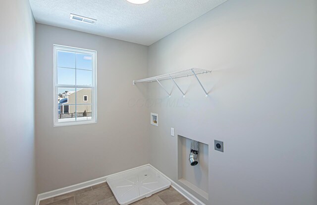 washroom featuring a textured ceiling, hookup for an electric dryer, hookup for a washing machine, and light tile patterned flooring