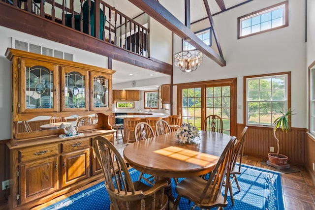 dining space featuring dark parquet flooring, french doors, a high ceiling, an inviting chandelier, and wood walls