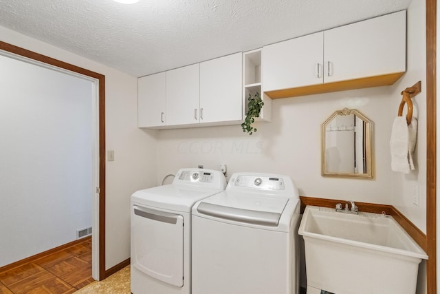 clothes washing area with a textured ceiling, washer and dryer, cabinets, and sink