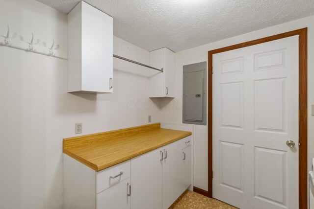 kitchen with white cabinets, a textured ceiling, and electric panel