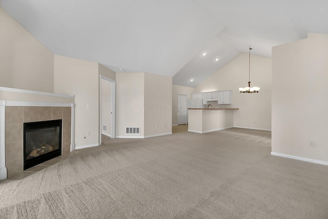 unfurnished living room featuring a tile fireplace, light colored carpet, an inviting chandelier, and lofted ceiling