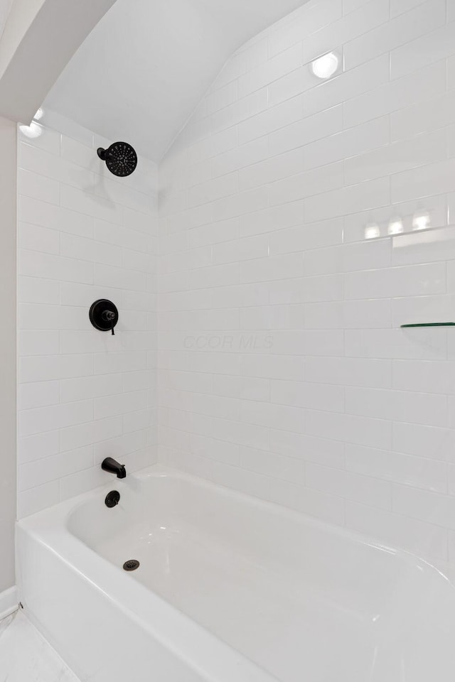 bathroom featuring vaulted ceiling and tiled shower / bath