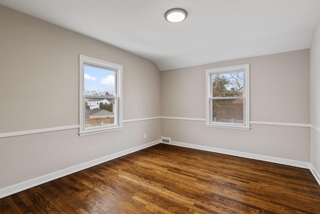 empty room featuring plenty of natural light, dark hardwood / wood-style flooring, and vaulted ceiling