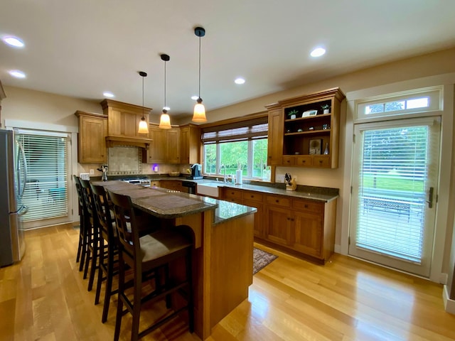 kitchen featuring light wood finished floors, brown cabinets, a breakfast bar, decorative light fixtures, and freestanding refrigerator