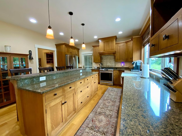 kitchen featuring a large island with sink, dark stone countertops, light hardwood / wood-style floors, decorative light fixtures, and appliances with stainless steel finishes