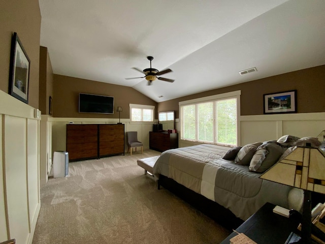 bedroom featuring a wainscoted wall, light colored carpet, vaulted ceiling, and ceiling fan