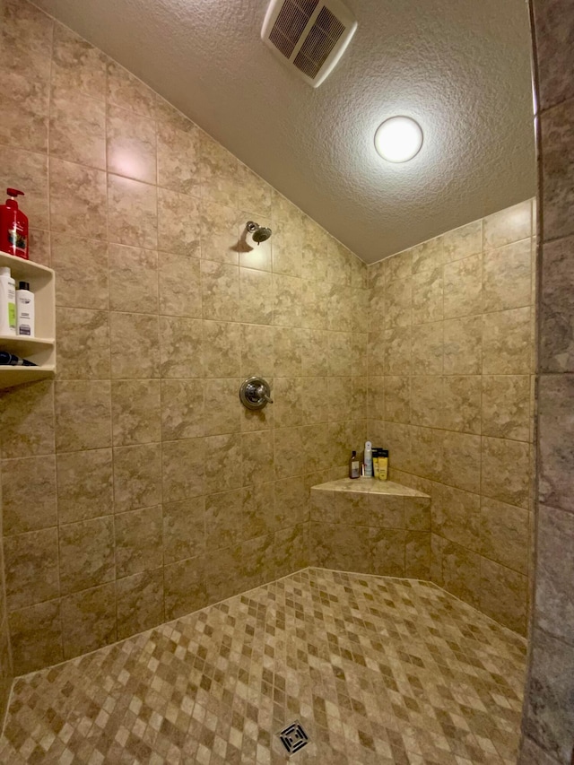 bathroom with a tile shower, a textured ceiling, and vaulted ceiling