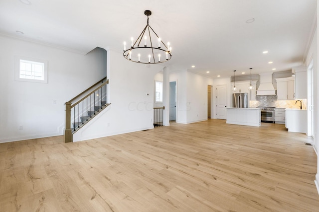 unfurnished living room with light hardwood / wood-style floors, an inviting chandelier, ornamental molding, and sink