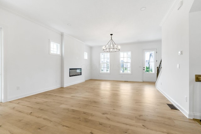 unfurnished living room with a chandelier, light wood-type flooring, and crown molding