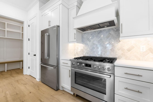 kitchen featuring white cabinetry, stainless steel appliances, tasteful backsplash, premium range hood, and light hardwood / wood-style floors