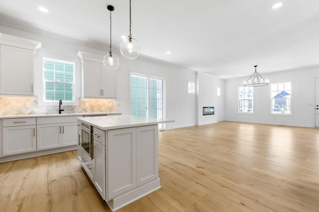 kitchen featuring a center island, sink, hanging light fixtures, decorative backsplash, and white cabinets