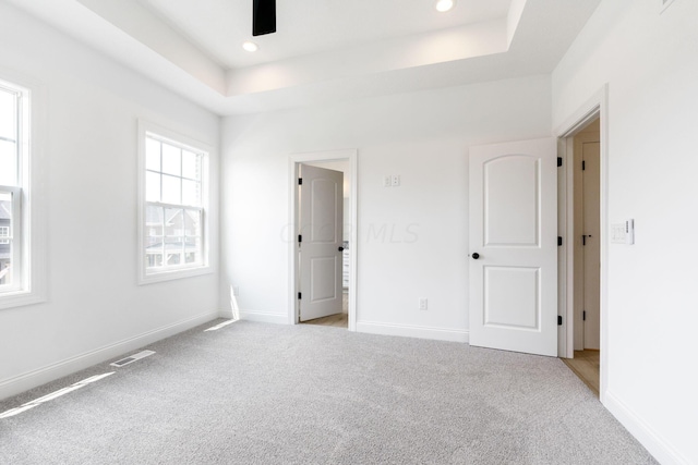 unfurnished bedroom featuring a raised ceiling and light carpet