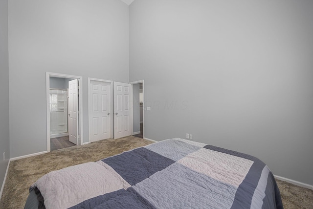 bedroom featuring a towering ceiling, connected bathroom, and dark carpet